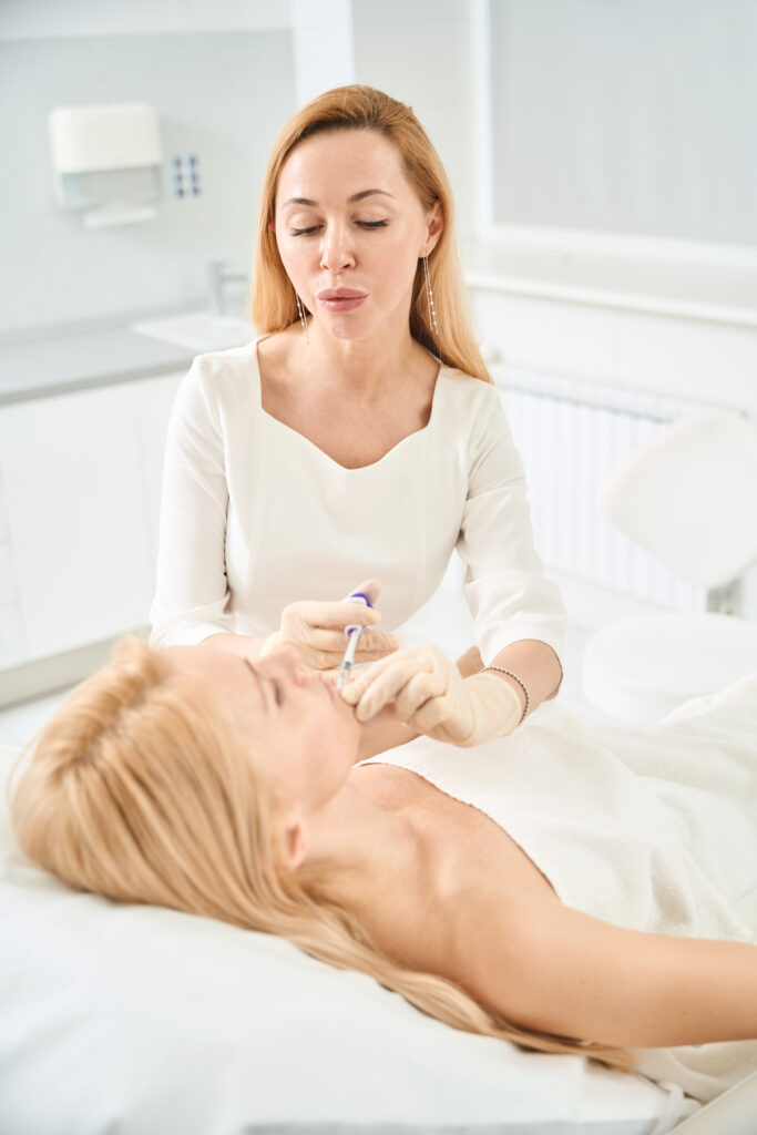 Concentrated dermatocosmetologist injecting filler into young woman chin