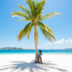 Woman standing in the shade of a palm tree on a tropical beach