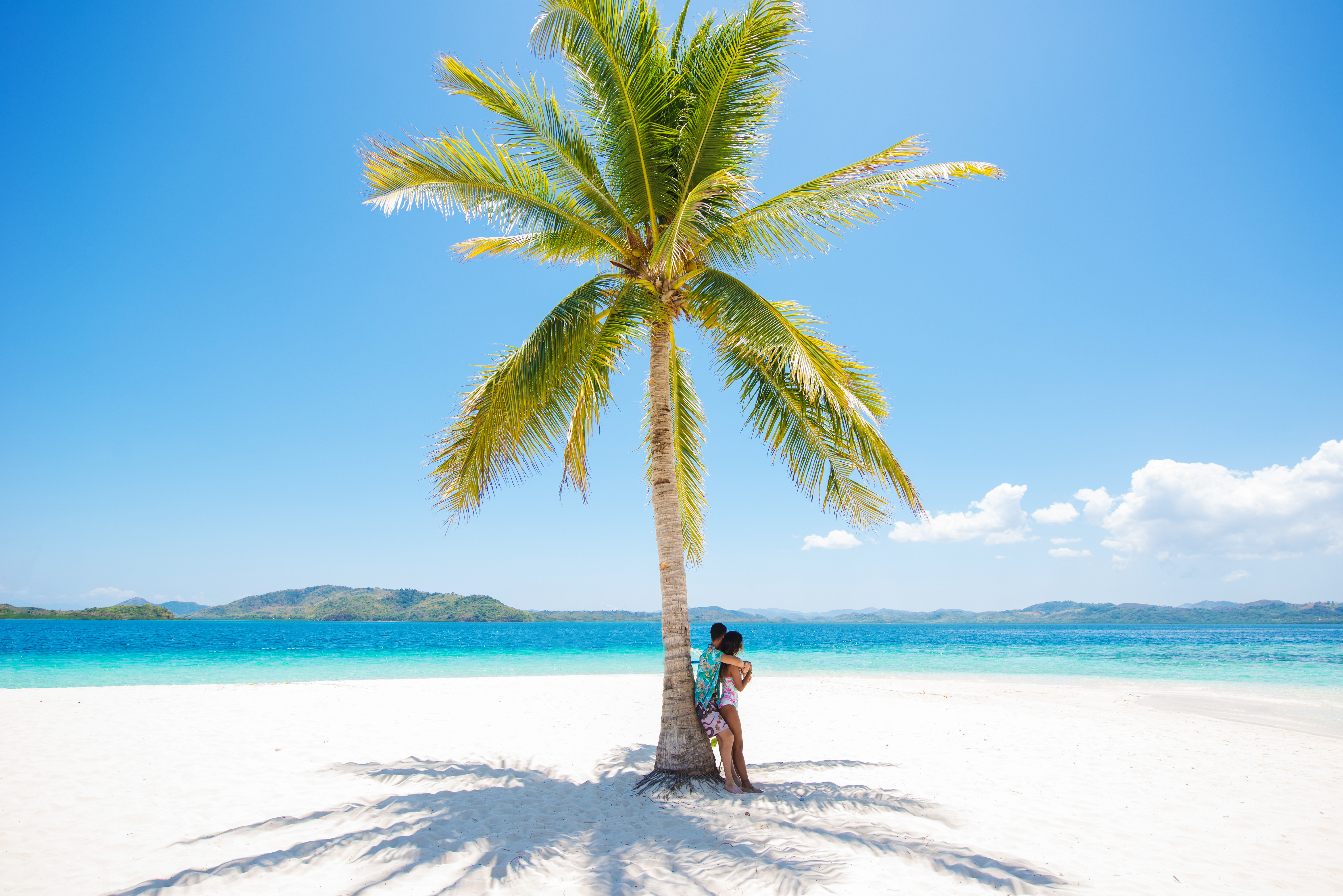 Woman standing in the shade of a palm tree on a tropical beach