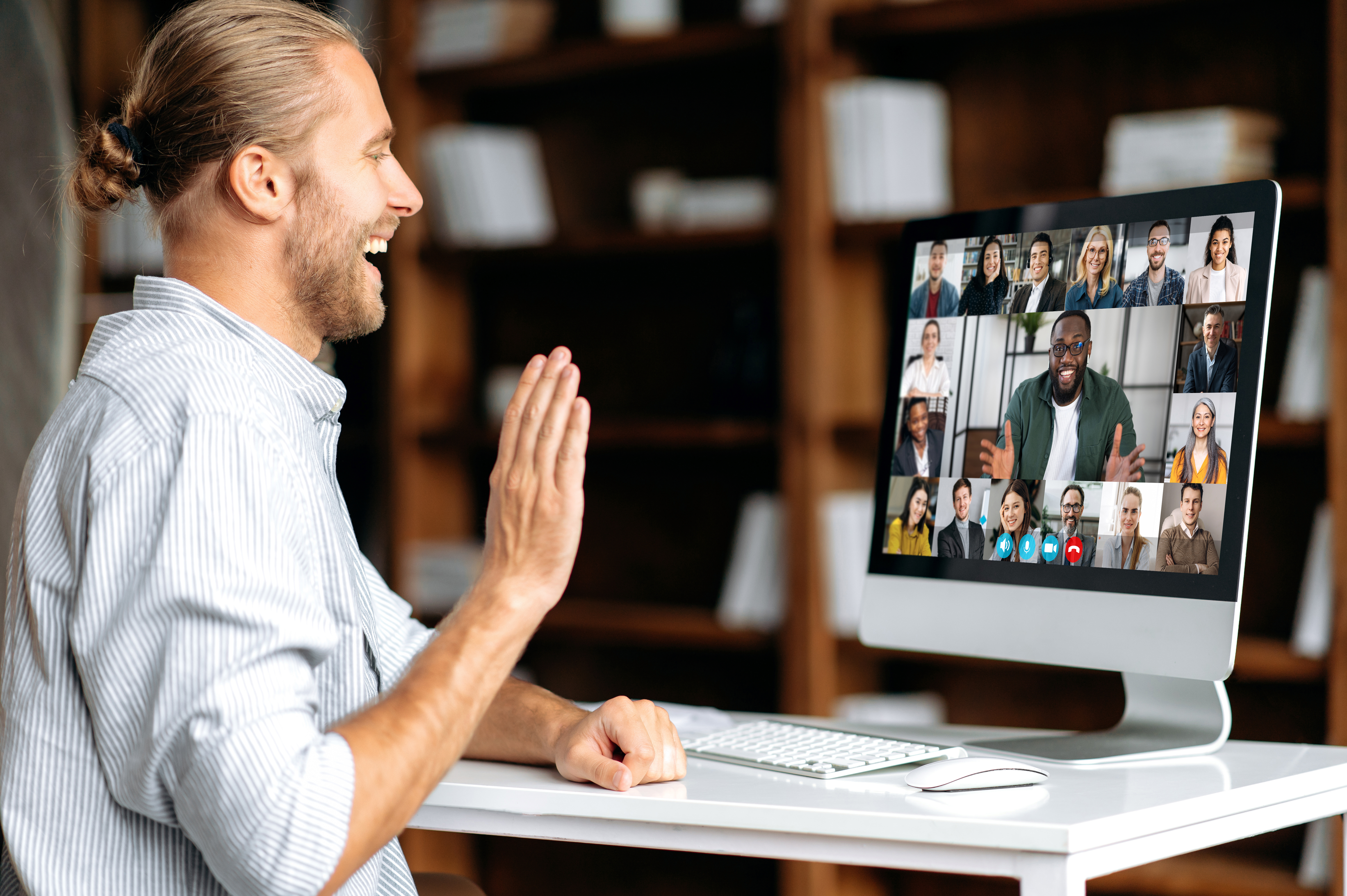 Man waving during a video call on desktop computer in a home office setting