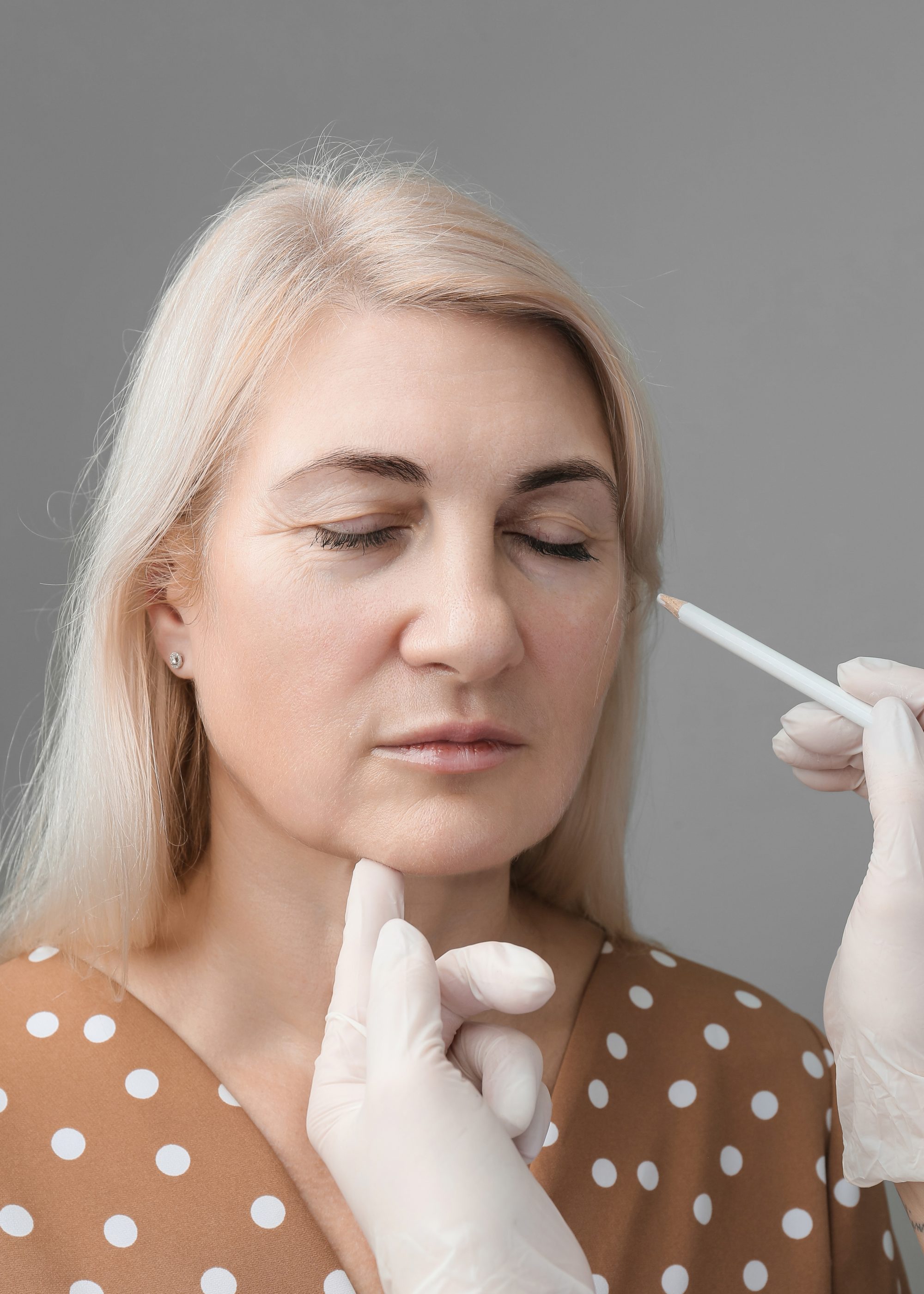 The beautician makes markings on the woman's face with a white pencil.