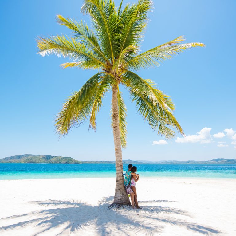 Woman standing in the shade of a palm tree on a tropical beach